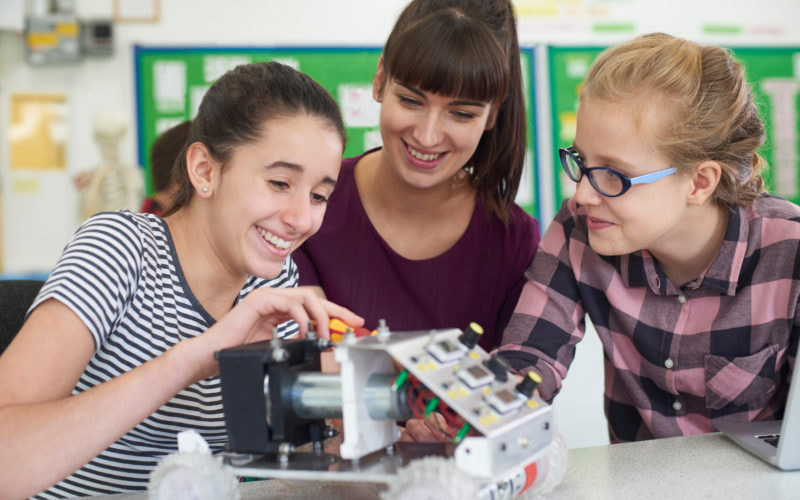 Teacher Talking To Female Pupils Studying Robotics In Science Lesson