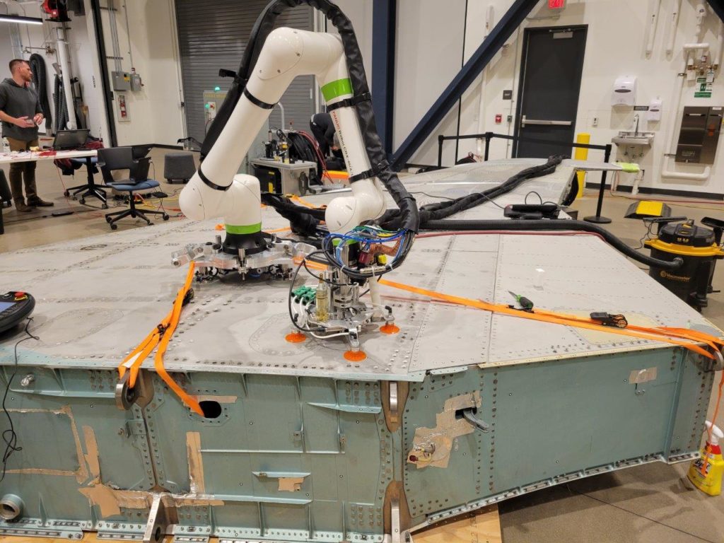 A close-up view of a collaborative robot sunctioned on to the wing of an F-15 completing a drilling task