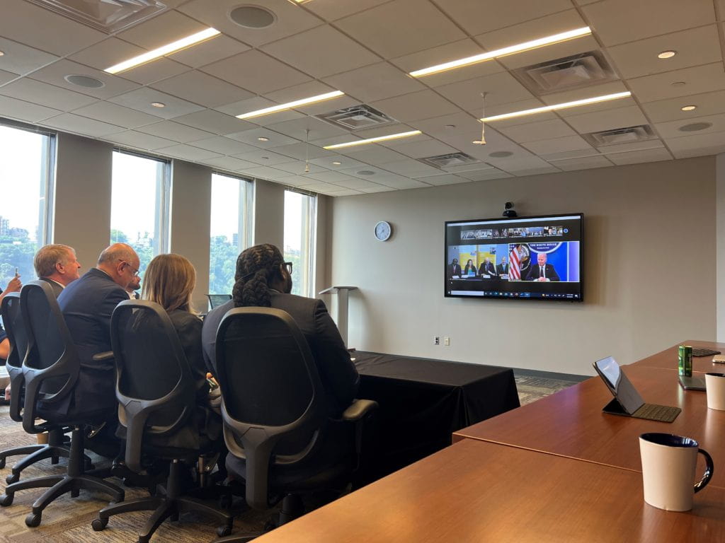 A room of people watch a Zoom screen
