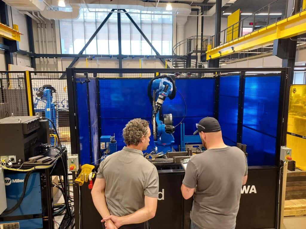 A group from Robinson Fans stands in front of Yaskawa's Robotic Welding Cell at the Robotics Manufacturing Hub