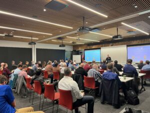 People gathered in a conference room watching presentations about robotic welding