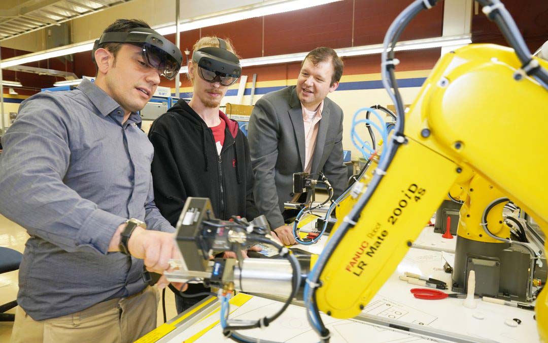 Justin Starr stands with two students and a robot arm