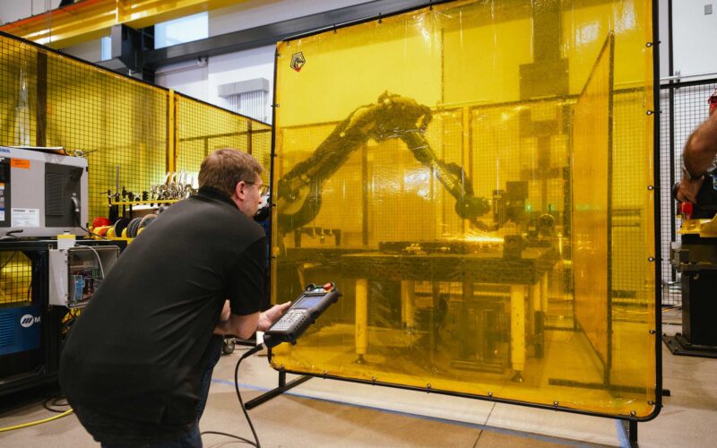 An image showing a man using a robot to grind a manufacturing part