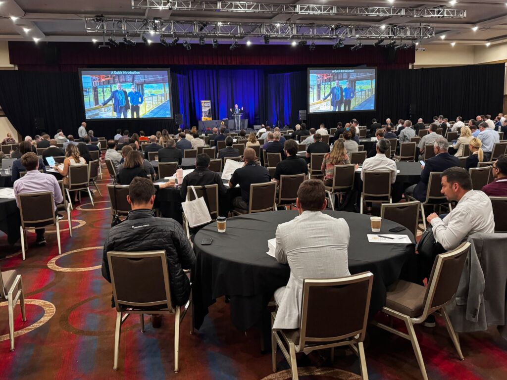 Attendees gather at tables and look at a screen during the Member Meeting